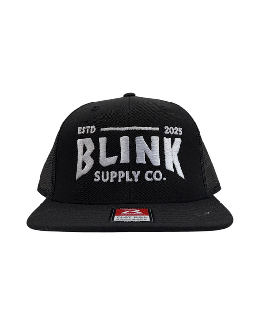 Blink Supply Co. black trucker hat with embroidered logo and flat bill. Features a snapback closure and mesh back panels.